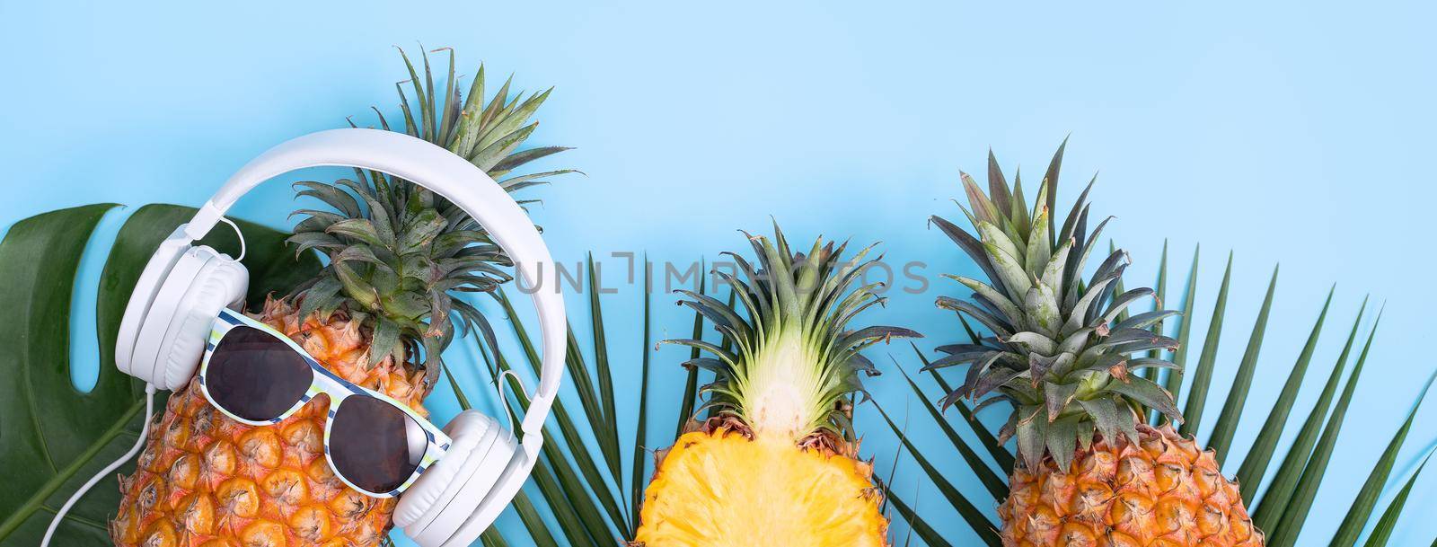 Funny pineapple wearing white headphone, concept of listening music, isolated on colored background with tropical palm leaves, top view, flat lay design. by ROMIXIMAGE