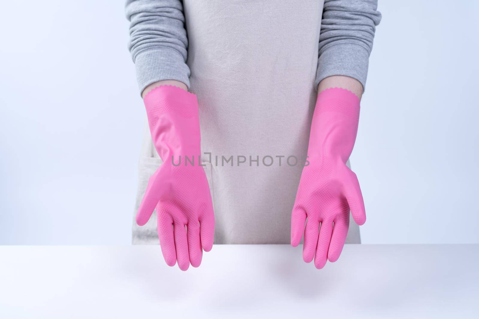Young woman housekeeper in apron is wearing pink gloves to clean the table, concept of preventing virus infection, housekeeping service, close up.