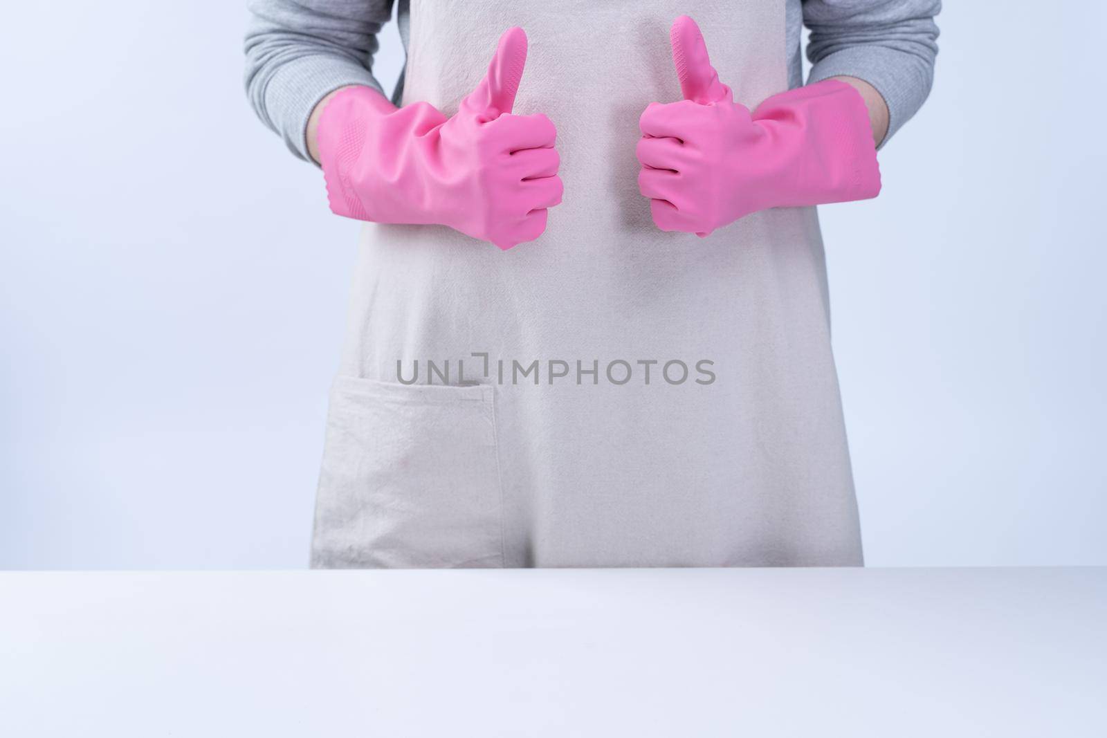 Young woman housekeeper in apron is wearing pink gloves to clean the table, concept of preventing virus infection, housekeeping service, close up.