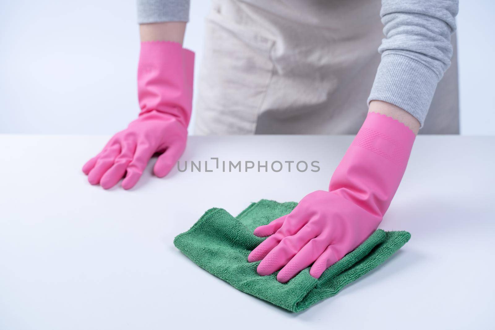 Young woman housekeeper in apron is wearing pink gloves to clean the table, concept of preventing virus infection, housekeeping service, close up.