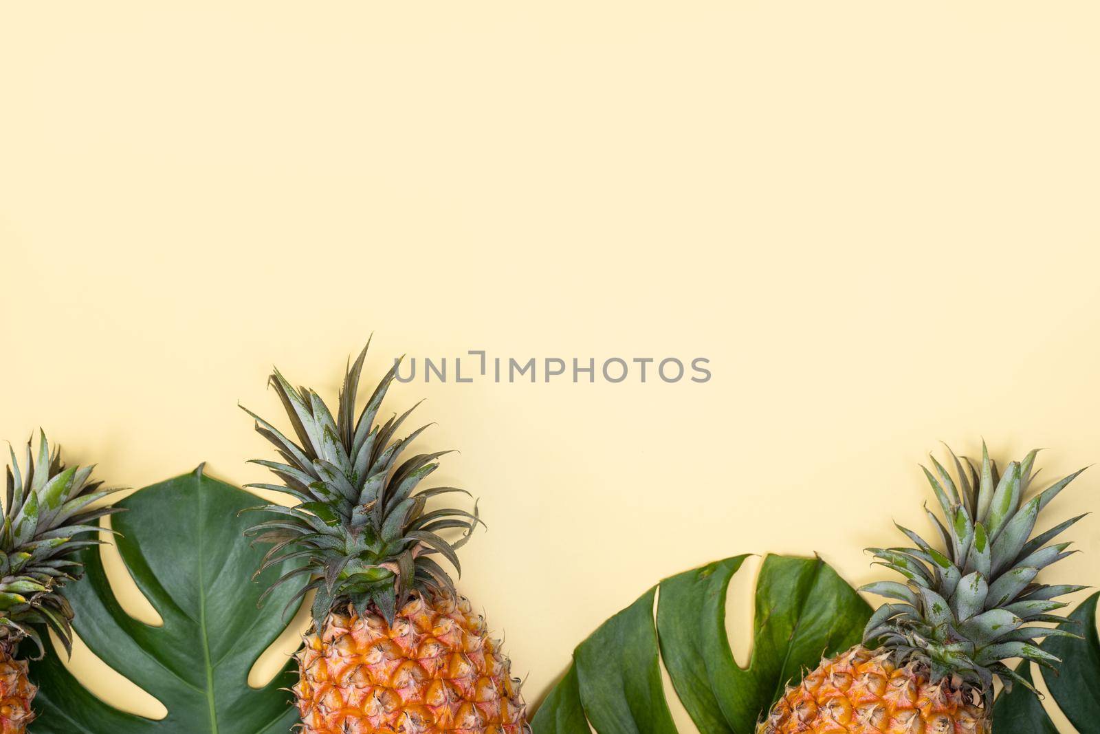 Beautiful pineapple on tropical palm monstera leaves isolated on bright pastel yellow background, top view, flat lay, overhead above summer fruit. by ROMIXIMAGE