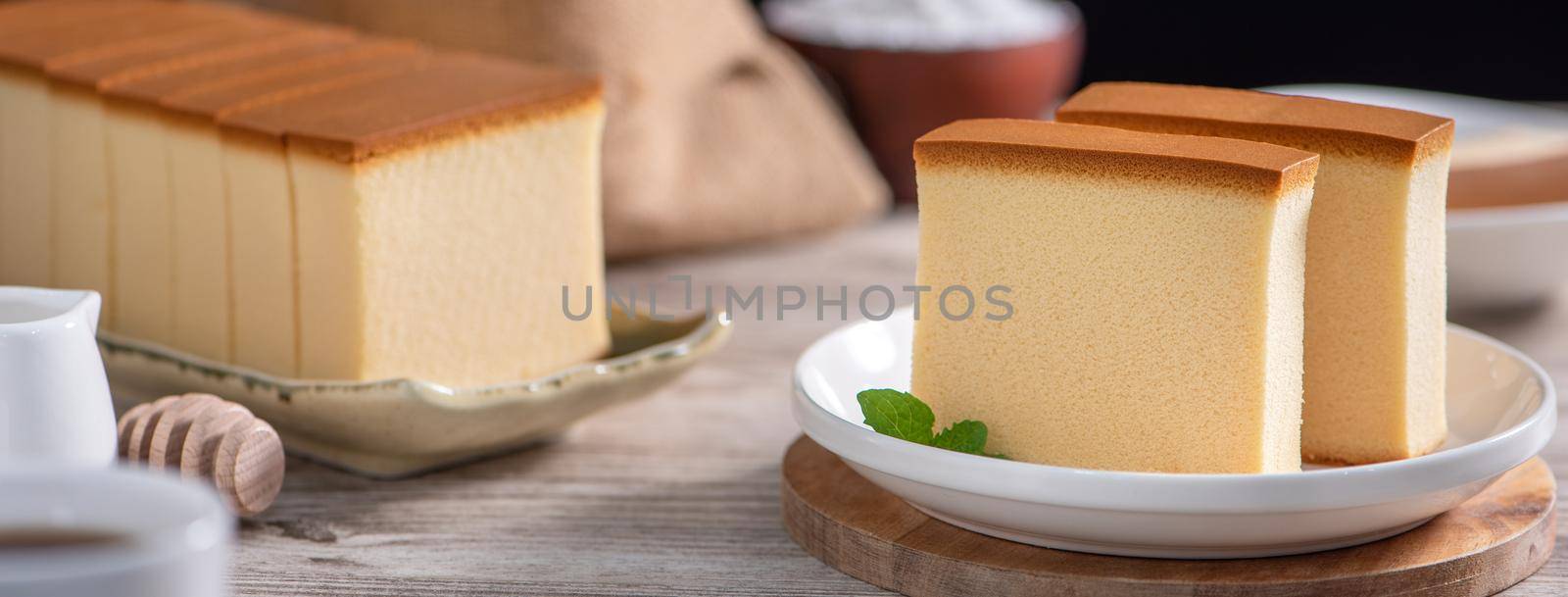Castella (kasutera) - Delicious Japanese sliced sponge cake food on white plate over rustic wooden table, close up, healthy eating, copy space design.