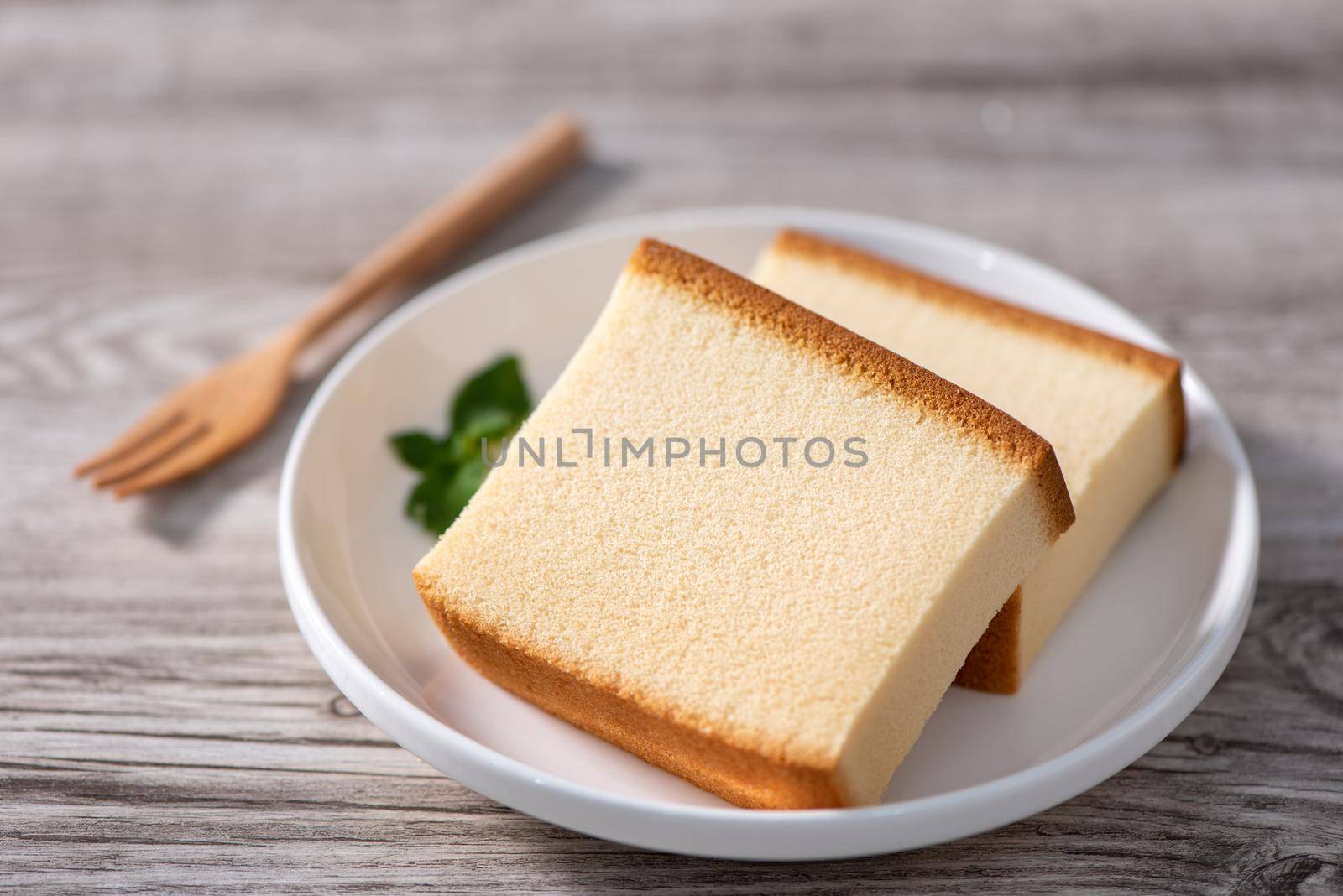 Castella (kasutera) - Delicious Japanese sliced sponge cake food on white plate over rustic wooden table, close up, healthy eating, copy space design.