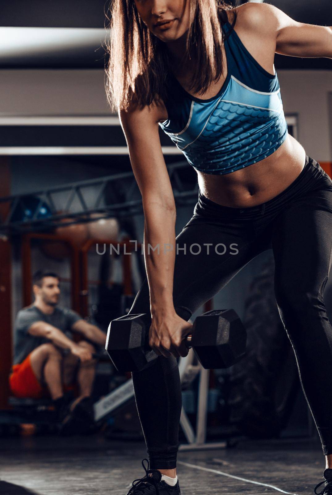 Young muscular cute woman doing hard exercise with dumbbell at the gym. 