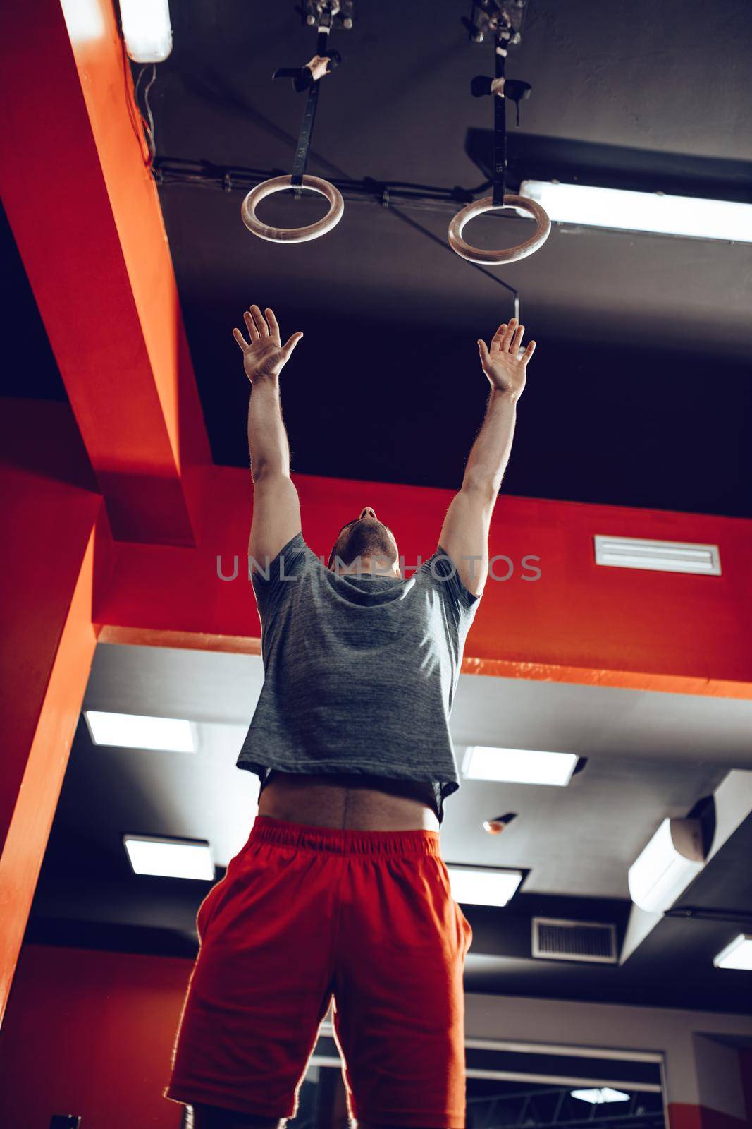 Young muscular man doing exercise on gymnast rings at the gym.