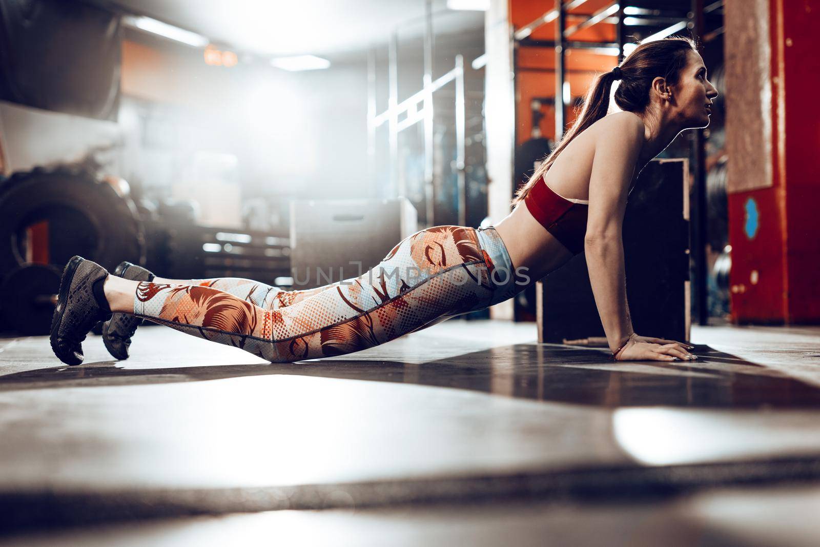 Attractive young muscular woman doing cross training at the gym. She is doing burpees exercise.