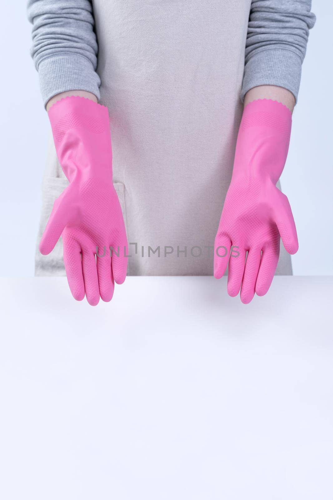 Young woman housekeeper in apron is wearing pink gloves to clean the table, concept of preventing virus infection, housekeeping service, close up.