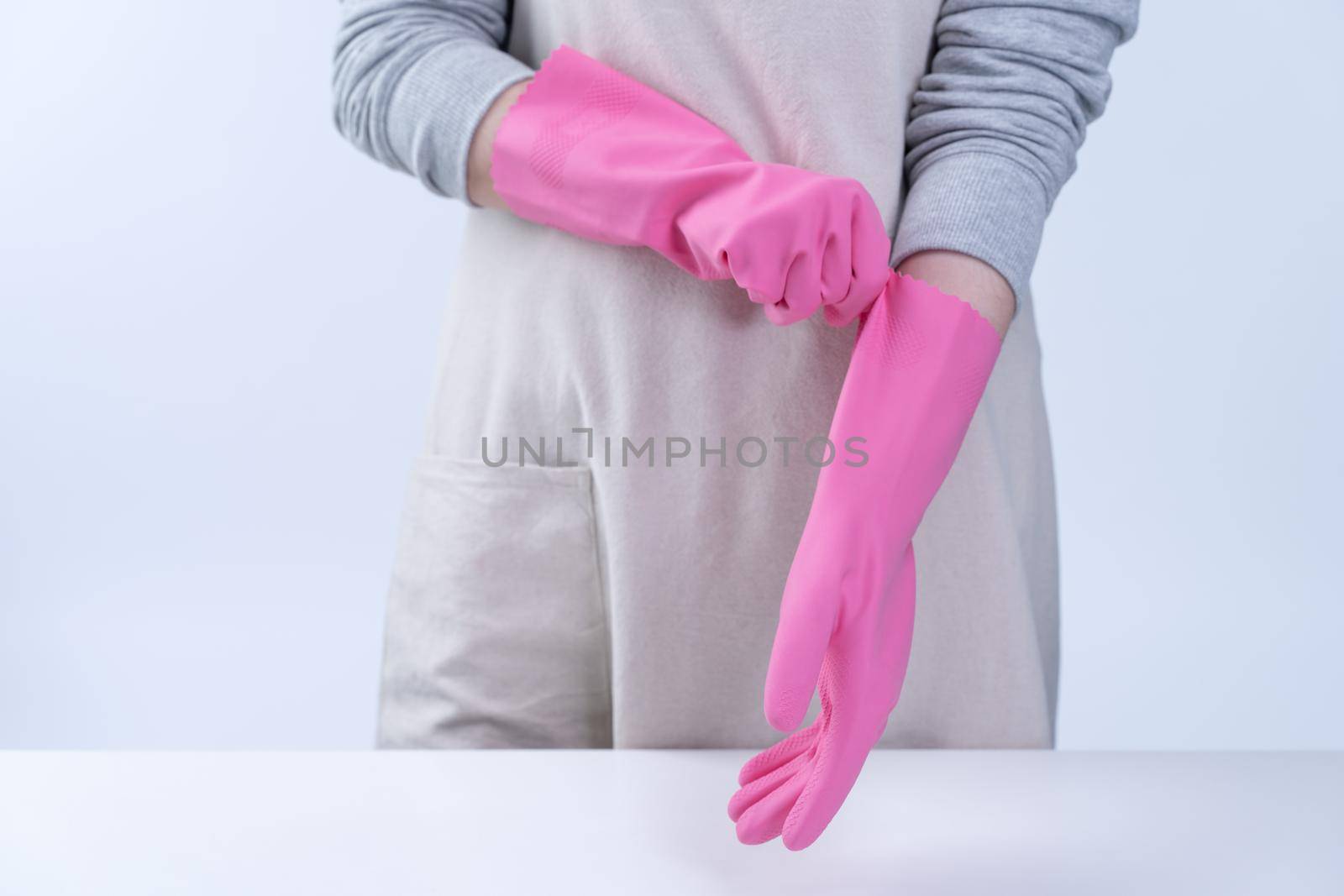 Young woman housekeeper in apron is wearing pink gloves to clean the table, concept of preventing virus infection, housekeeping service, close up.