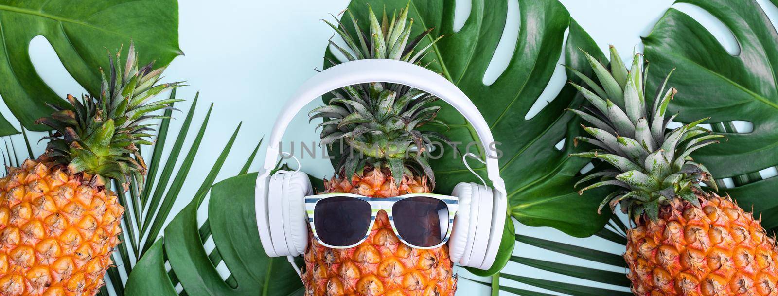 Funny pineapple wearing white headphone, concept of listening music, isolated on colored background with tropical palm leaves, top view, flat lay design. by ROMIXIMAGE