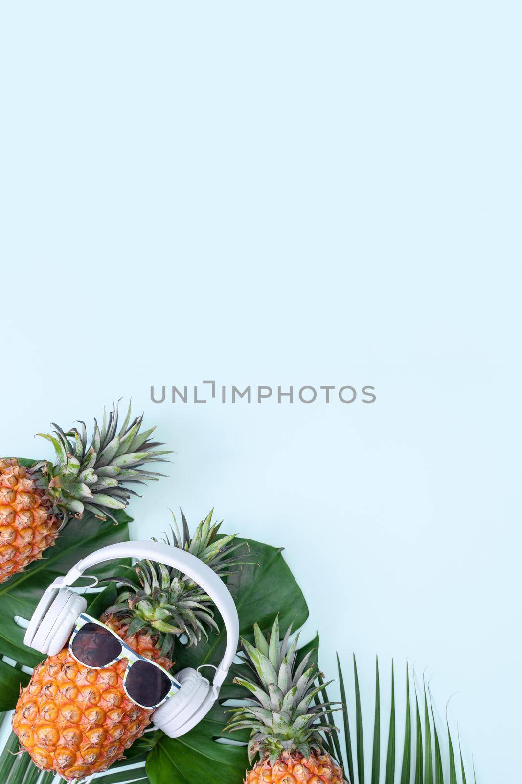 Funny pineapple wearing white headphone, concept of listening music, isolated on colored background with tropical palm leaves, top view, flat lay design.