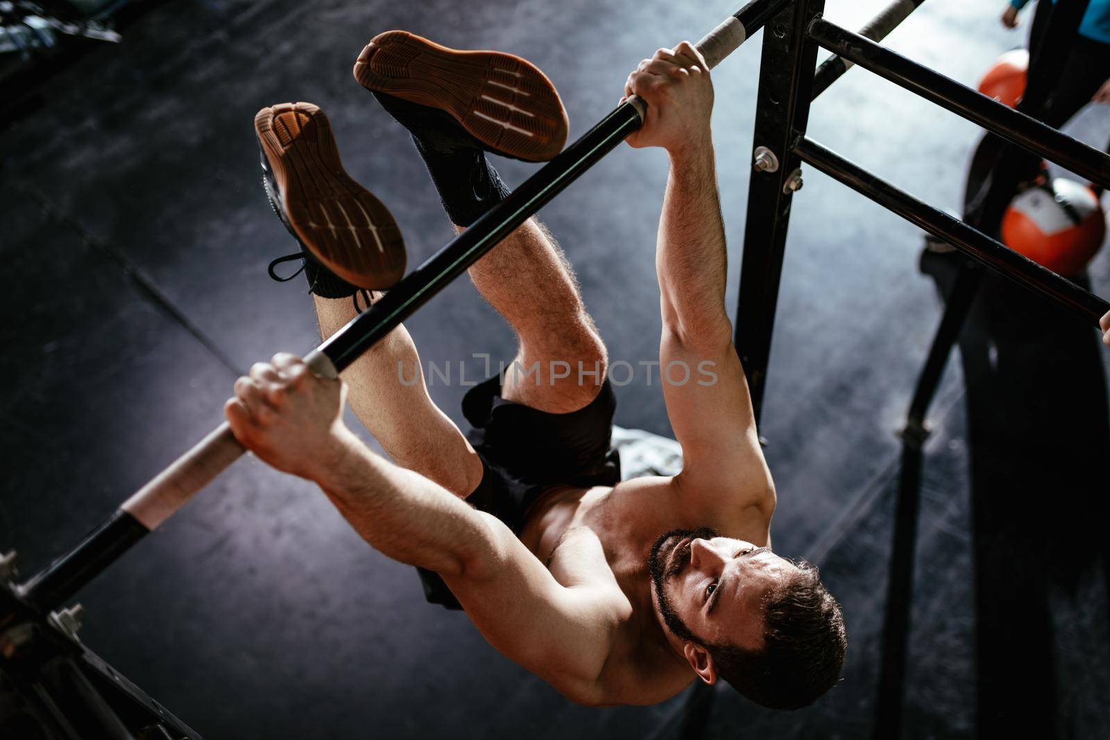 Strong young muscular man doing toes to bar exercise at the gym. 