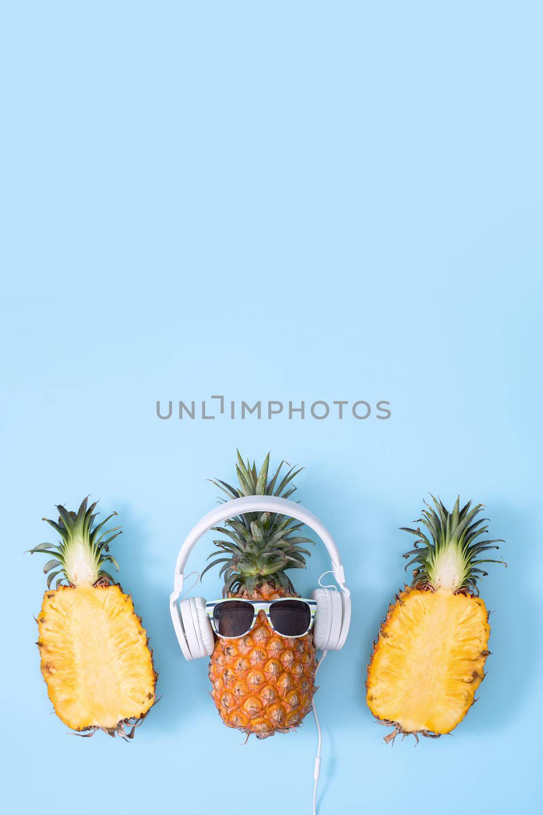 Funny pineapple wearing white headphone, concept of listening music, isolated on colored background with tropical palm leaves, top view, flat lay design.