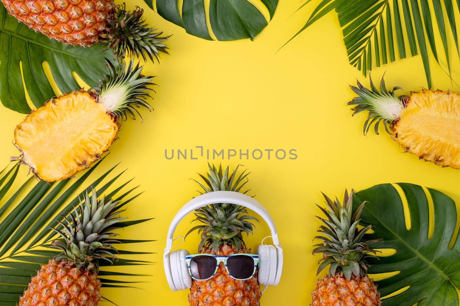 Funny pineapple wearing white headphone, listen music, isolated on yellow background with tropical palm leaves, top view, flat lay design concept. by ROMIXIMAGE