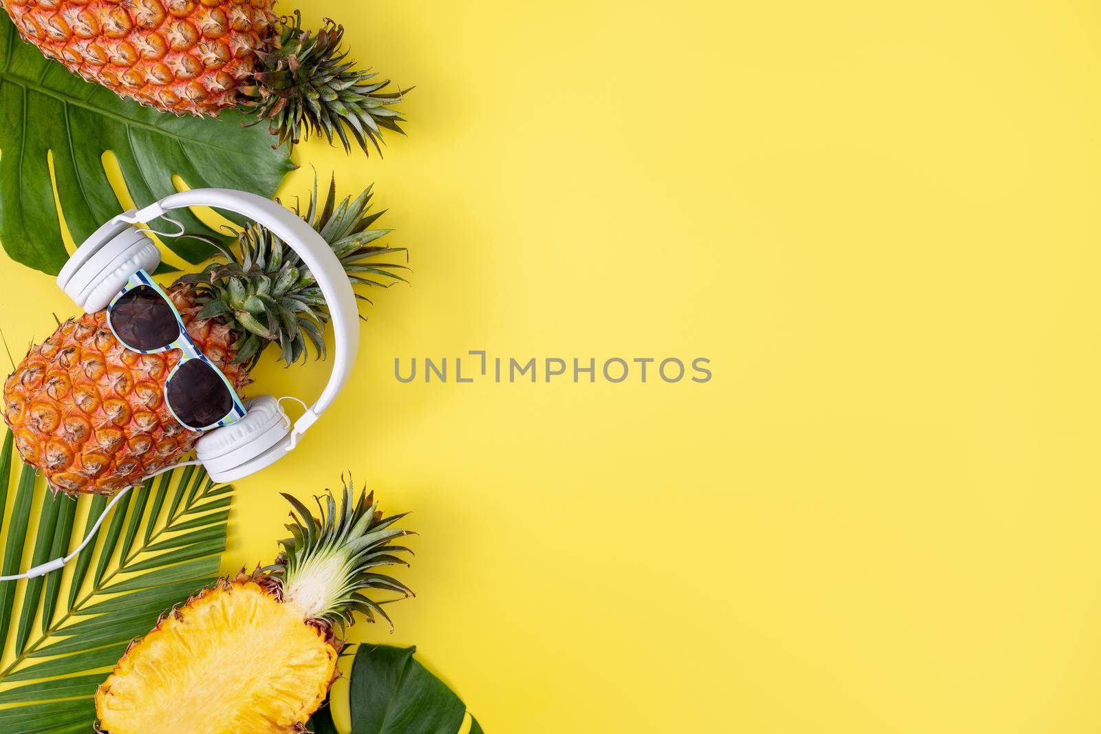 Funny pineapple wearing white headphone, listen music, isolated on yellow background with tropical palm leaves, top view, flat lay design concept. by ROMIXIMAGE