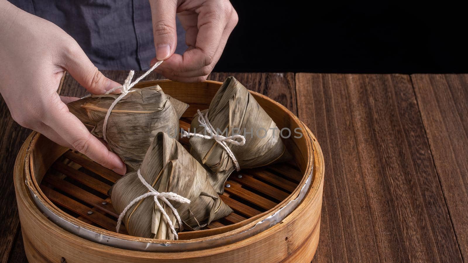 Rice dumpling, zongzi - Dragon Boat Festival, Bunch of Chinese traditional cooked food in steamer on wooden table over black background, close up, copy space