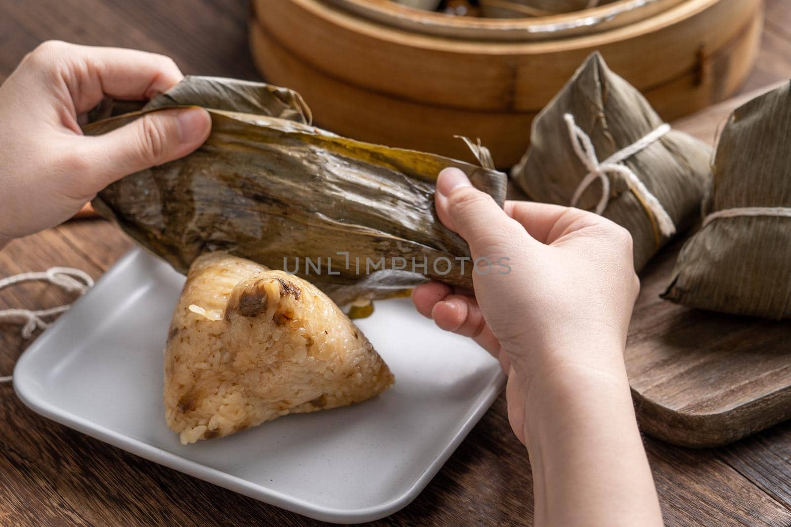 Eating zongzi - Dragon Boat Festival Rice dumpling young Asian woman eating Chinese traditional food on wooden table at home celebration, close up