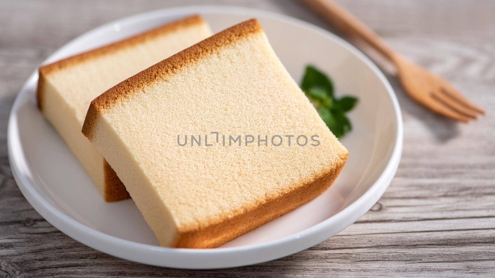 Castella - Delicious Japanese sliced sponge cake food on white plate over rustic wooden table, close up, healthy eating, copy space design.