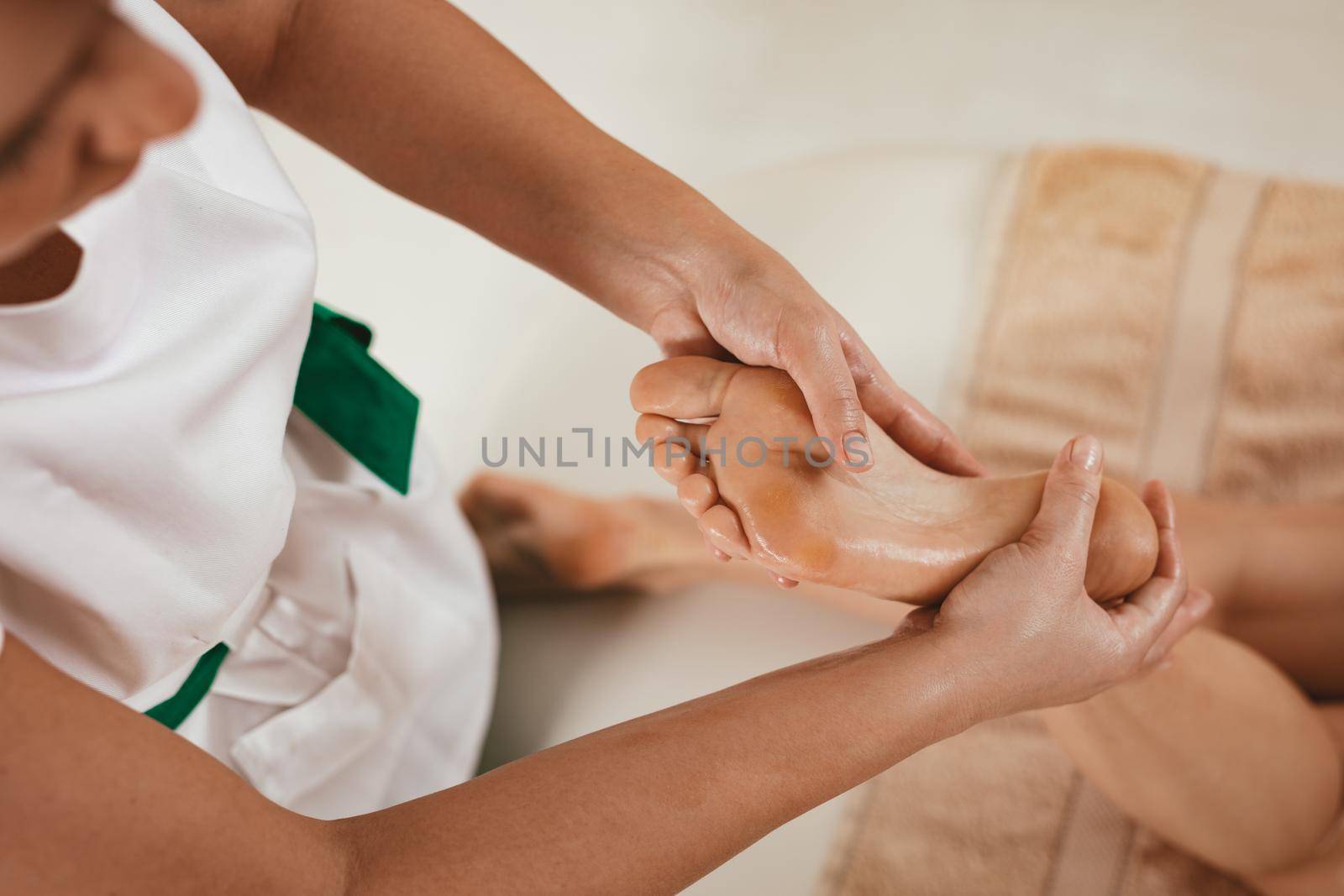 Close-up of a young female therapist massaging young woman's foot at beauty salon.