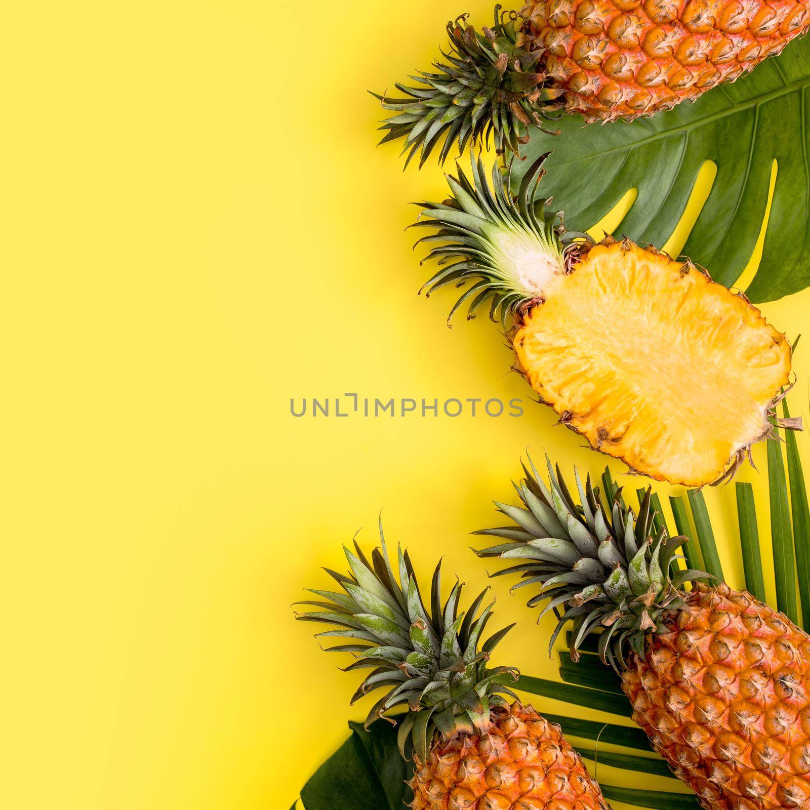 Beautiful pineapple on tropical palm monstera leaves isolated on bright pastel yellow background, top view, flat lay, overhead above summer fruit.