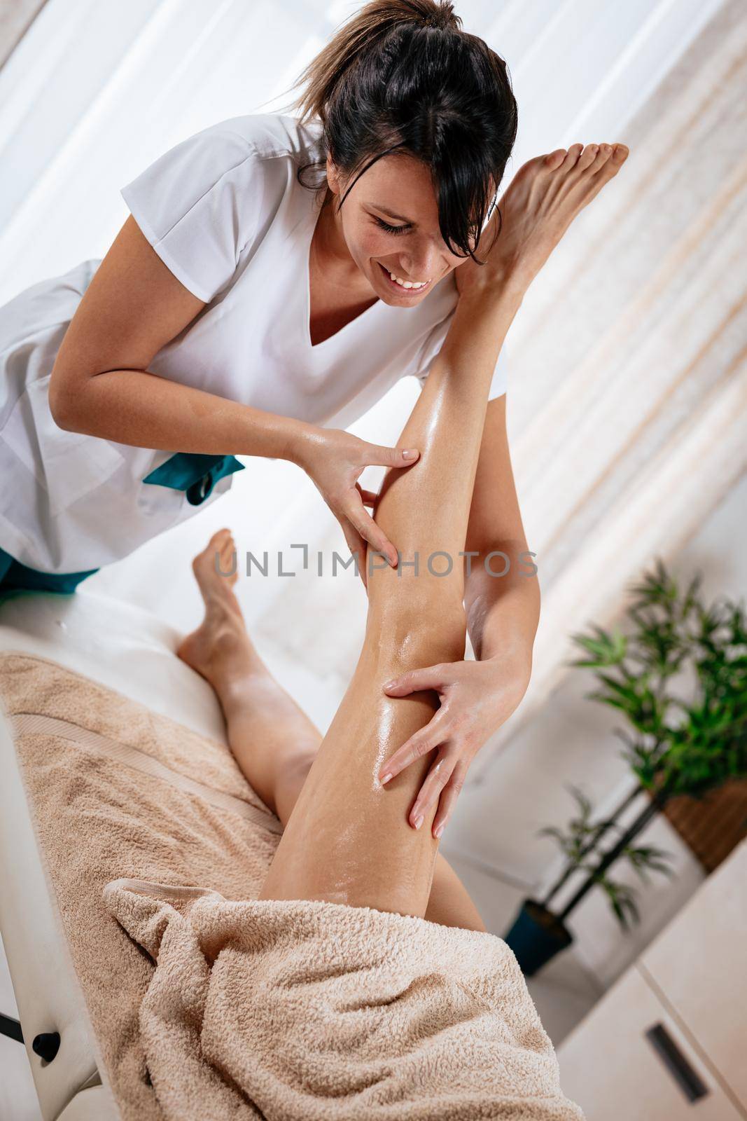Beautiful smiling female therapist massaging young woman's leg at beauty salon. 