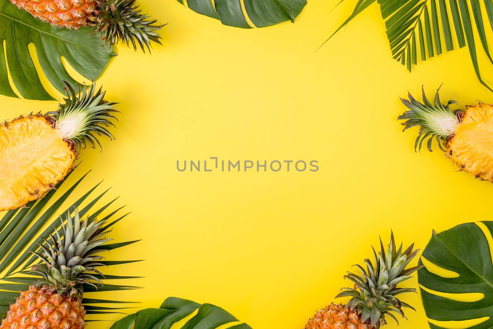 Beautiful pineapple on tropical palm monstera leaves isolated on bright pastel yellow background, top view, flat lay, overhead above summer fruit.