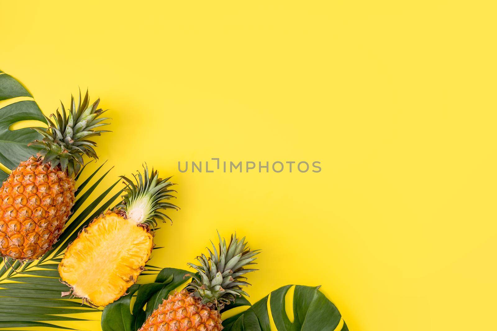 Beautiful pineapple on tropical palm monstera leaves isolated on bright pastel yellow background, top view, flat lay, overhead above summer fruit. by ROMIXIMAGE