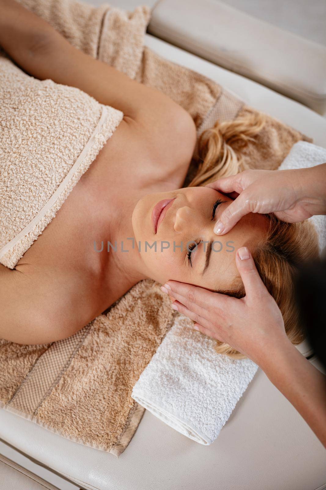 Close-up of a beautiful healthy young woman enjoying relaxing facial massage at beauty salon. Top view.