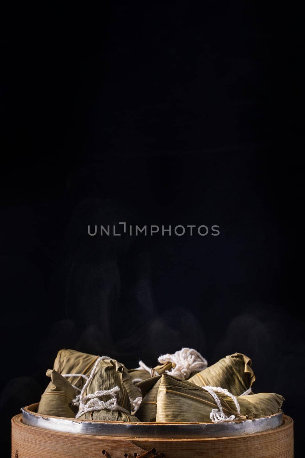 Rice dumpling, zongzi - Dragon Boat Festival, Bunch of Chinese traditional cooked food in steamer on wooden table over black background, close up, copy space