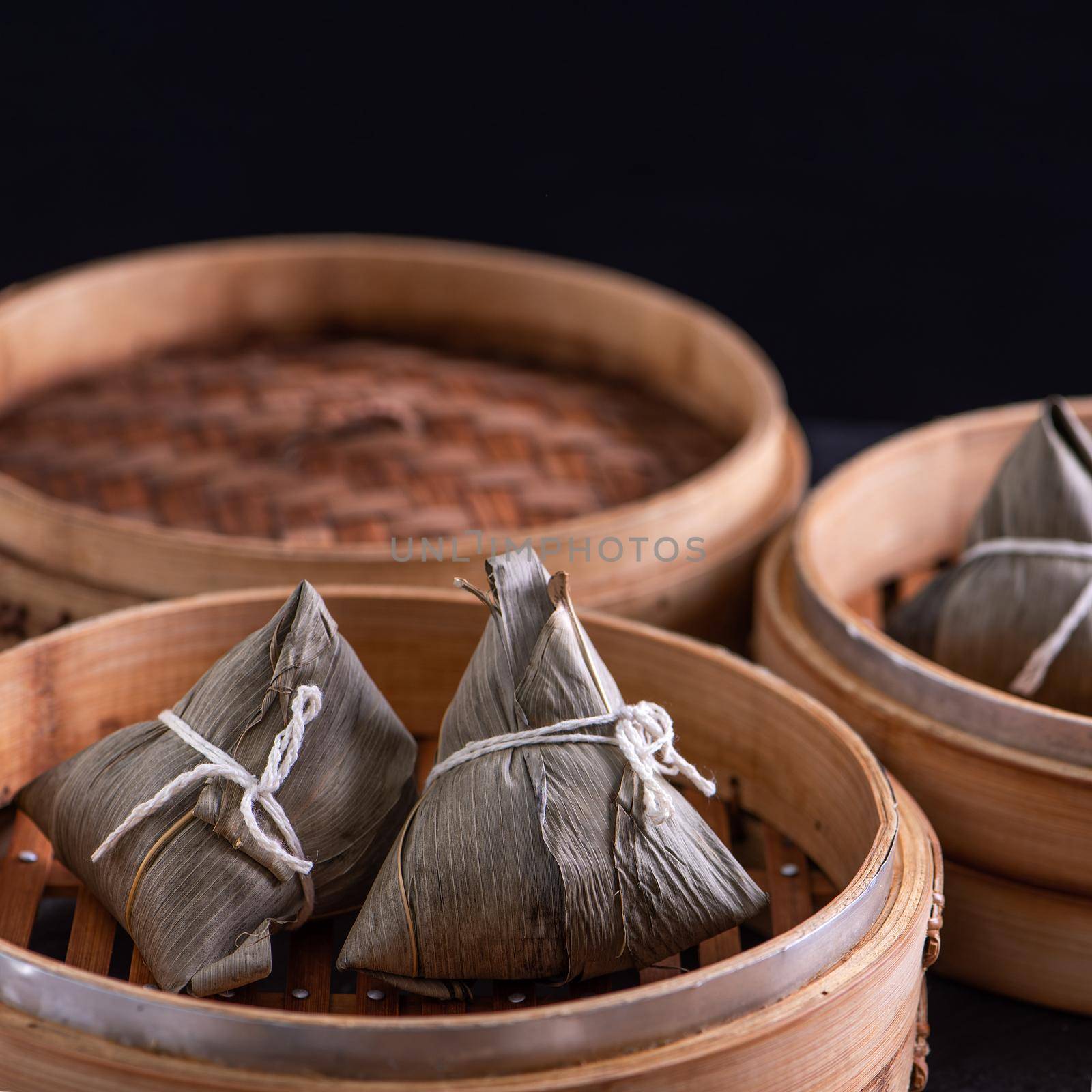 Rice dumpling, zongzi - Dragon Boat Festival, Bunch of Chinese traditional cooked food in steamer on wooden table over black background, close up, copy space