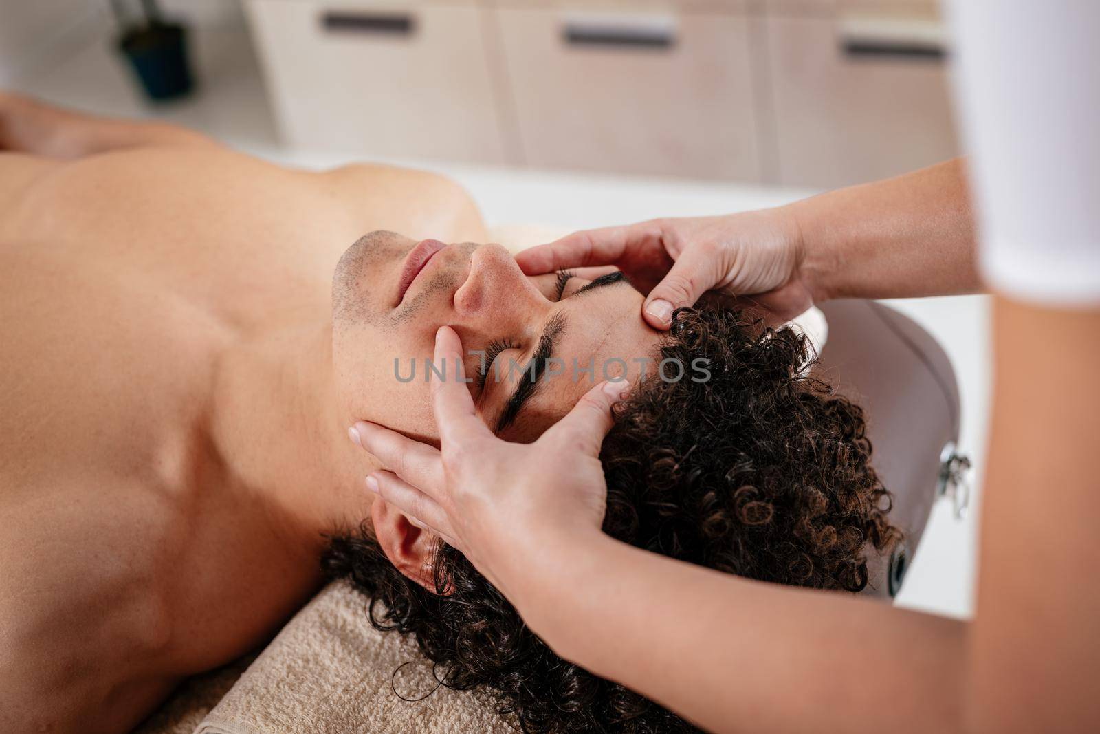 Close-up of a handsome healthy young man enjoying relaxing facial massage at beauty salon.