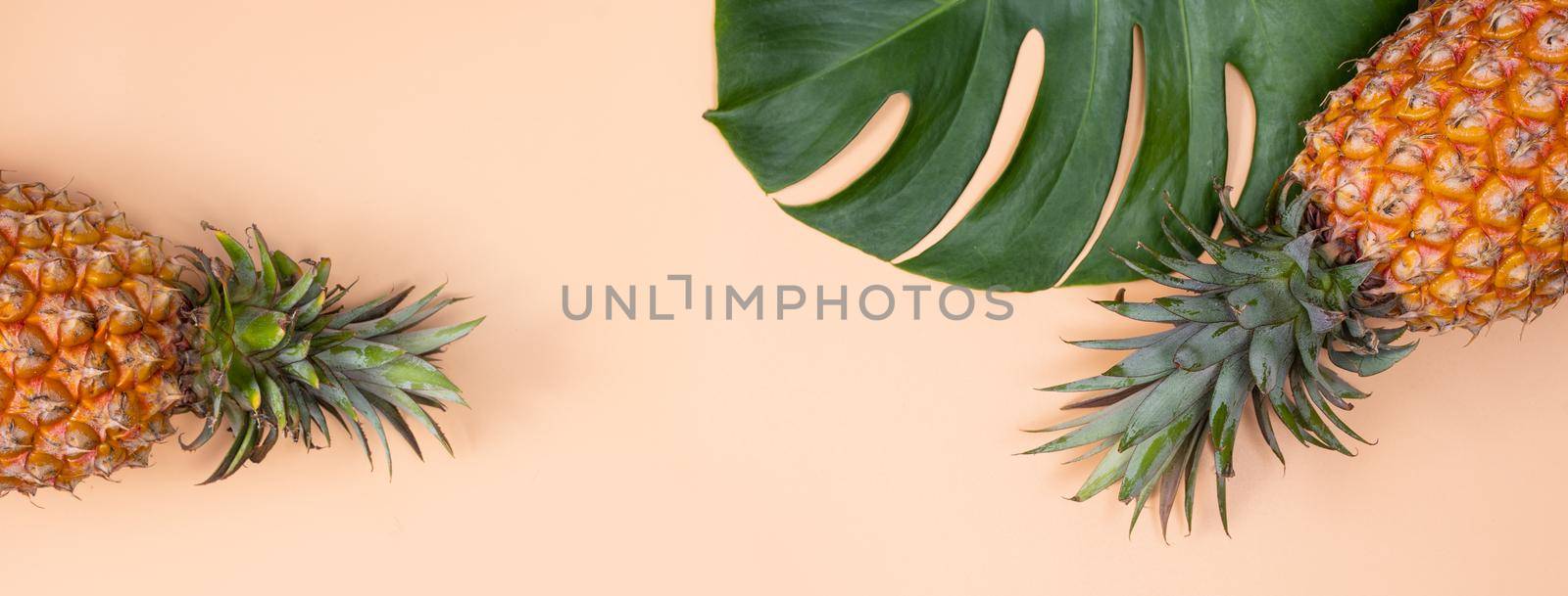 Beautiful pineapple on tropical palm monstera leaves isolated on bright pastel orange yellow background, top view, flat lay, overhead above summer fruit.