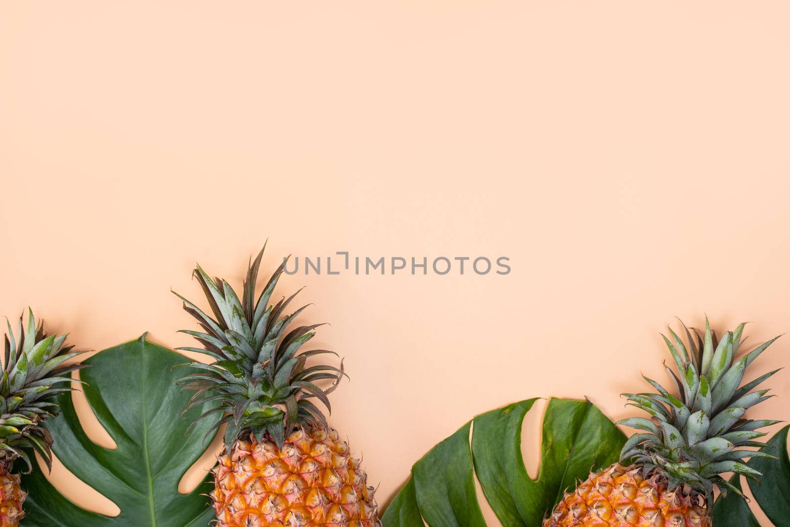 Beautiful pineapple on tropical palm monstera leaves isolated on bright pastel orange yellow background, top view, flat lay, overhead above summer fruit.