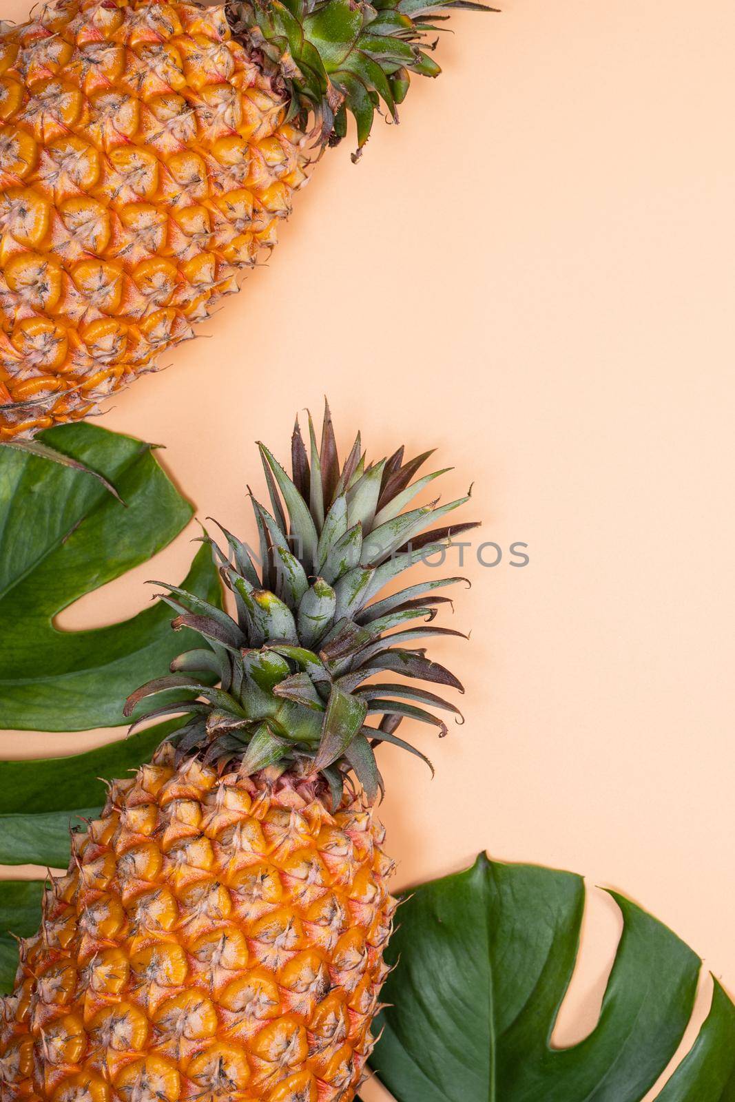 Beautiful pineapple on tropical palm monstera leaves isolated on bright pastel orange yellow background, top view, flat lay, overhead above summer fruit.