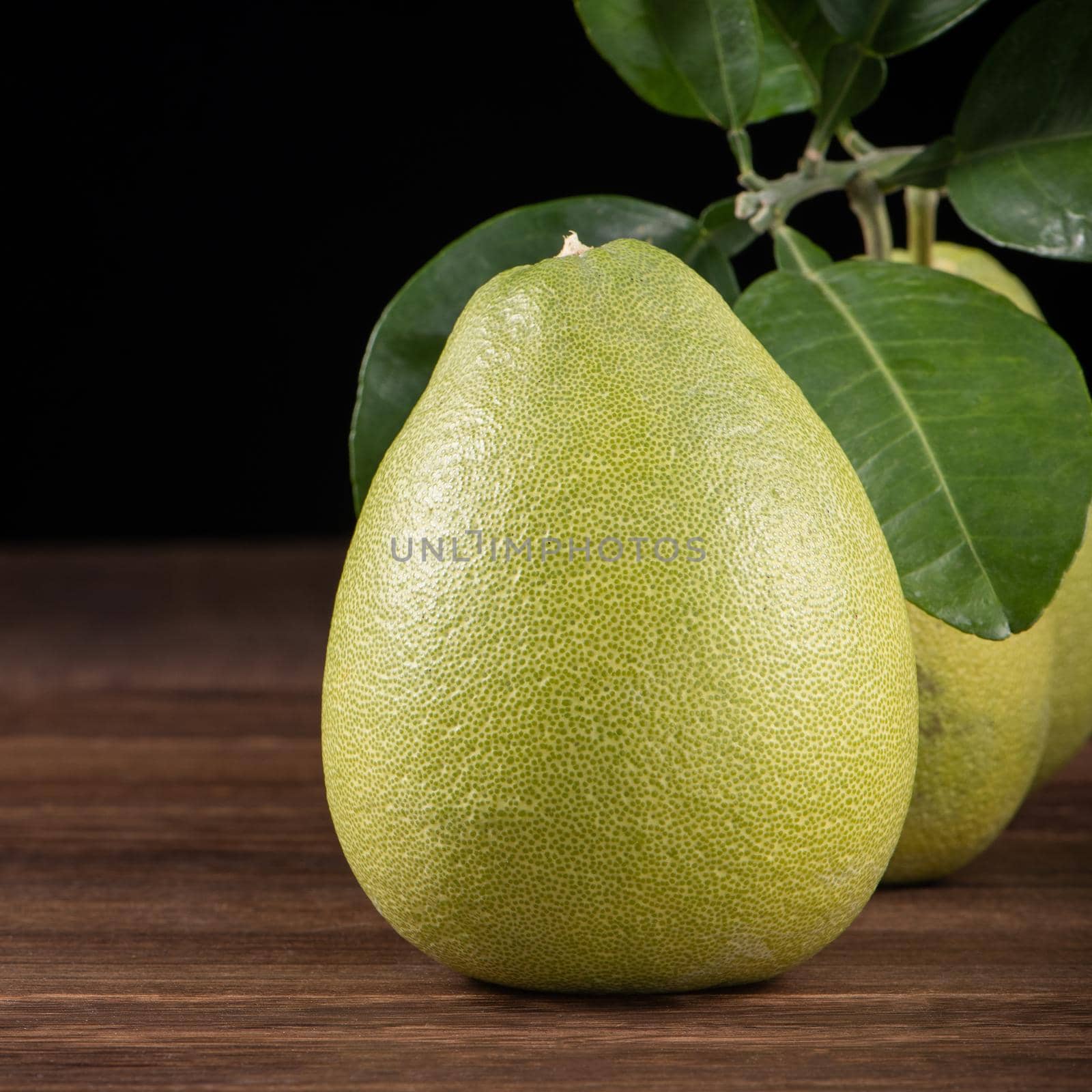 Fresh pomelo, pummelo, grapefruit, shaddock on wooden table over black background, close up, copy space. Fruit for Mid-autumn festival.