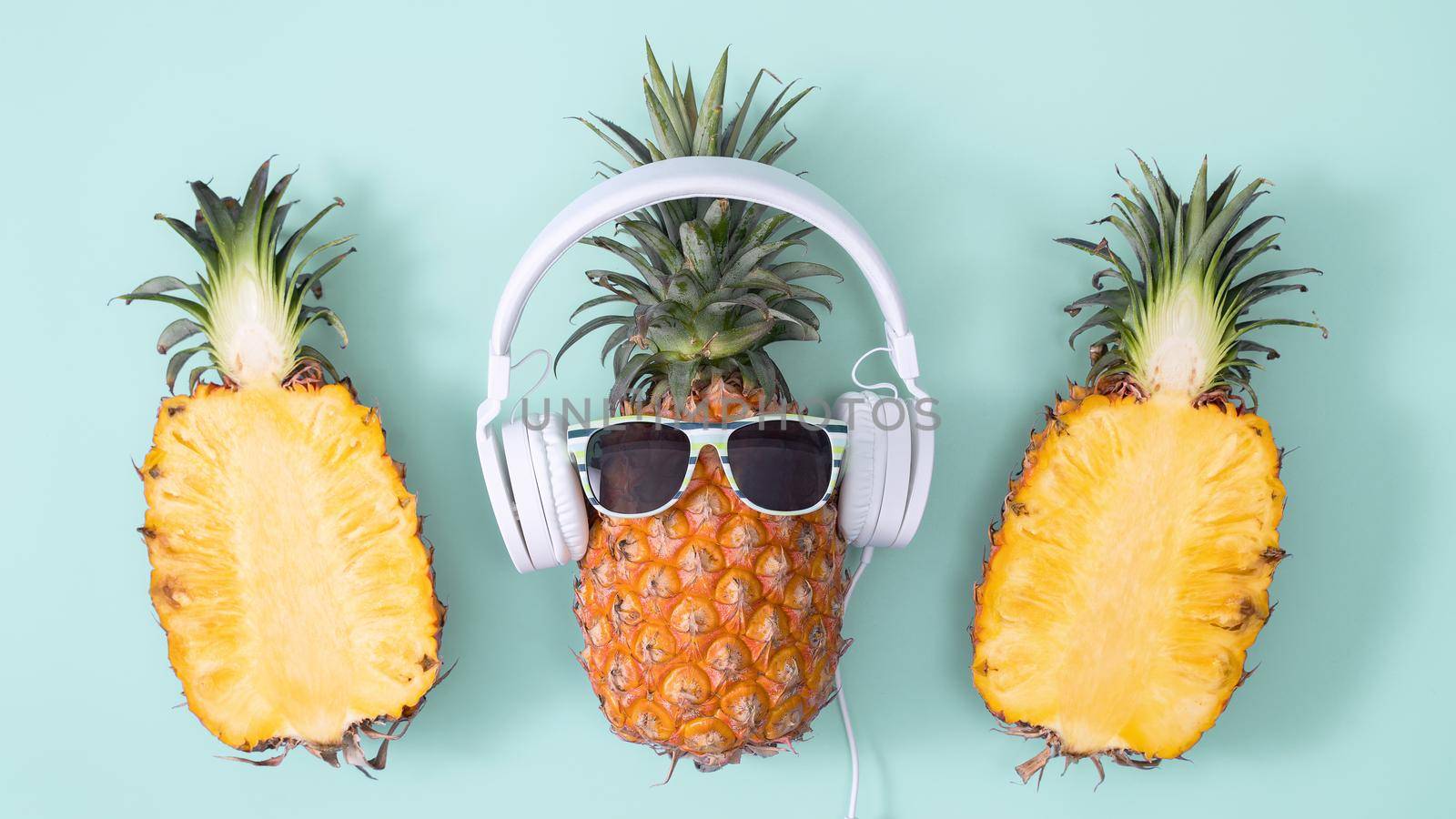 Funny pineapple wearing white headphone, concept of listening music, isolated on colored background with tropical palm leaves, top view, flat lay design. by ROMIXIMAGE