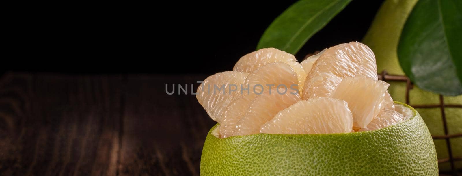 Fresh pomelo, pummelo, grapefruit, shaddock on wooden table over black background, close up, copy space. Fruit for Mid-autumn festival. by ROMIXIMAGE