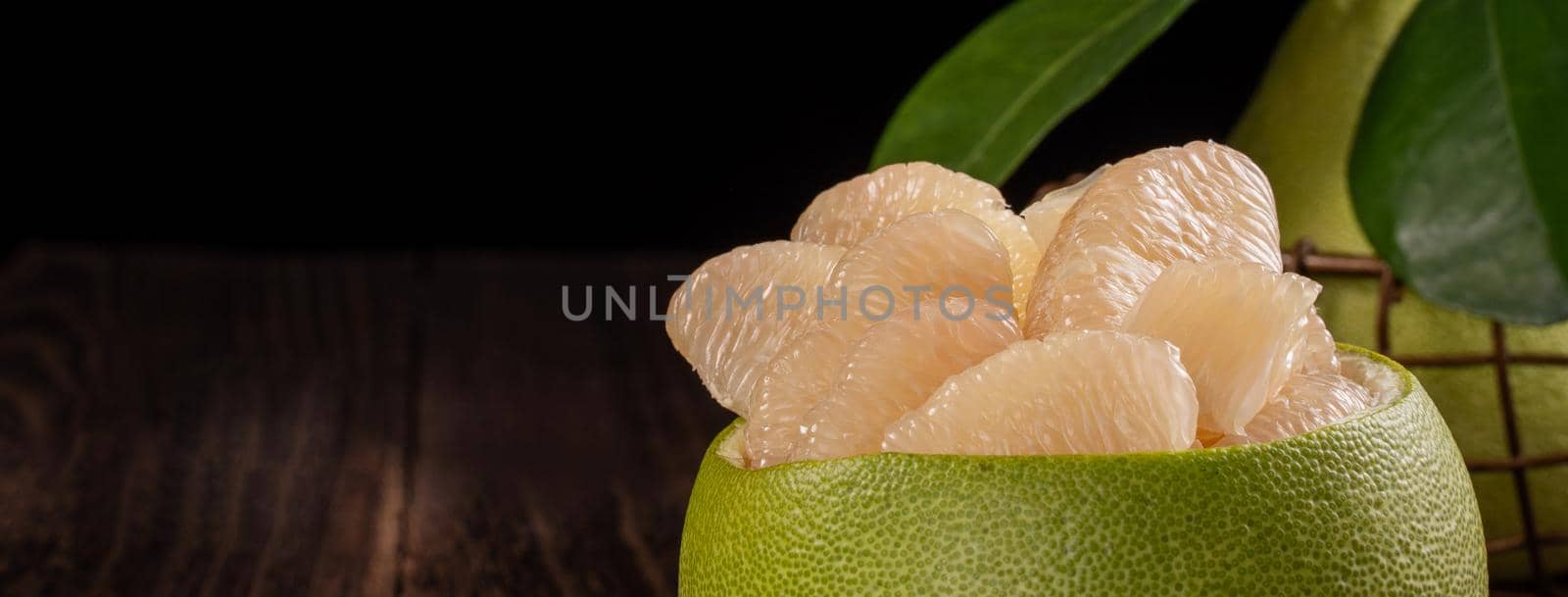 Fresh pomelo, pummelo, grapefruit, shaddock on wooden table over black background, close up, copy space. Fruit for Mid-autumn festival.