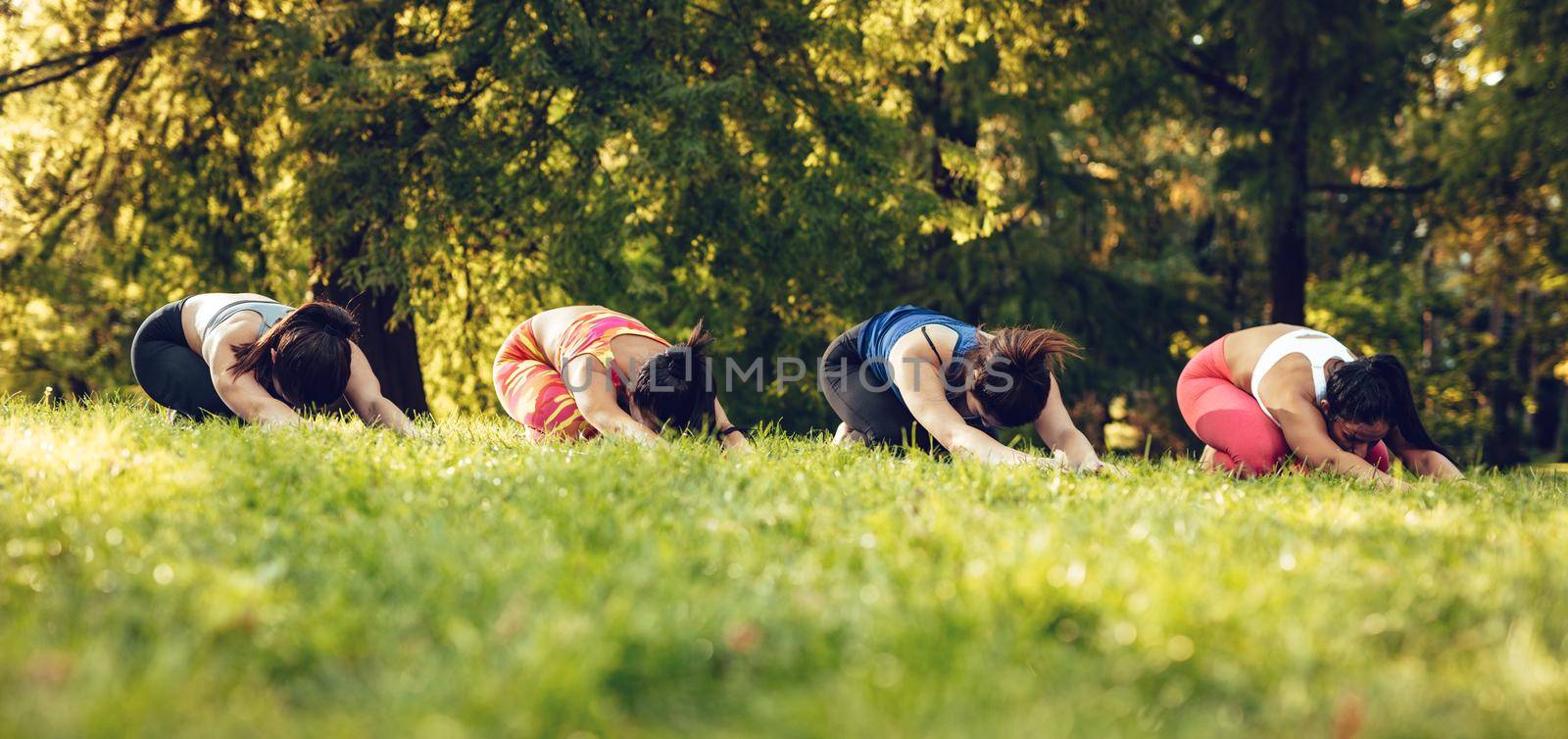 Four beautiful motivated female friends doing stretching exercise in the city park.