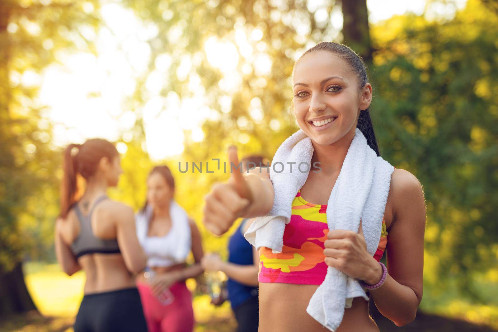 Beautiful sporty happy smiling woman relaxing after doing stretching exercise in the city park. Looking at camera.