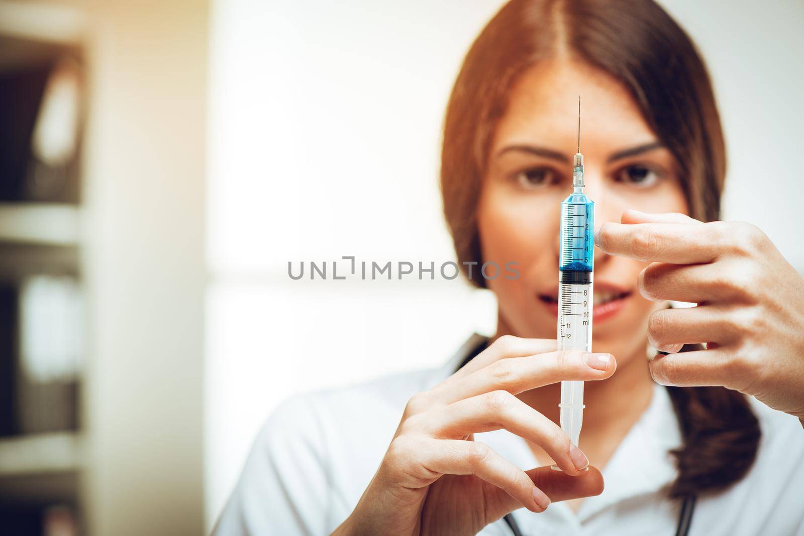 Young female nurse standing in her consulting room and preparing an injection of Anesthesia. Selective focus. Focus on foreground, on injection.