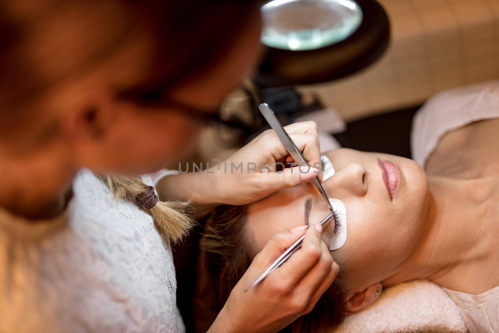 Beautician applying extended eyelashes to model. Top view.