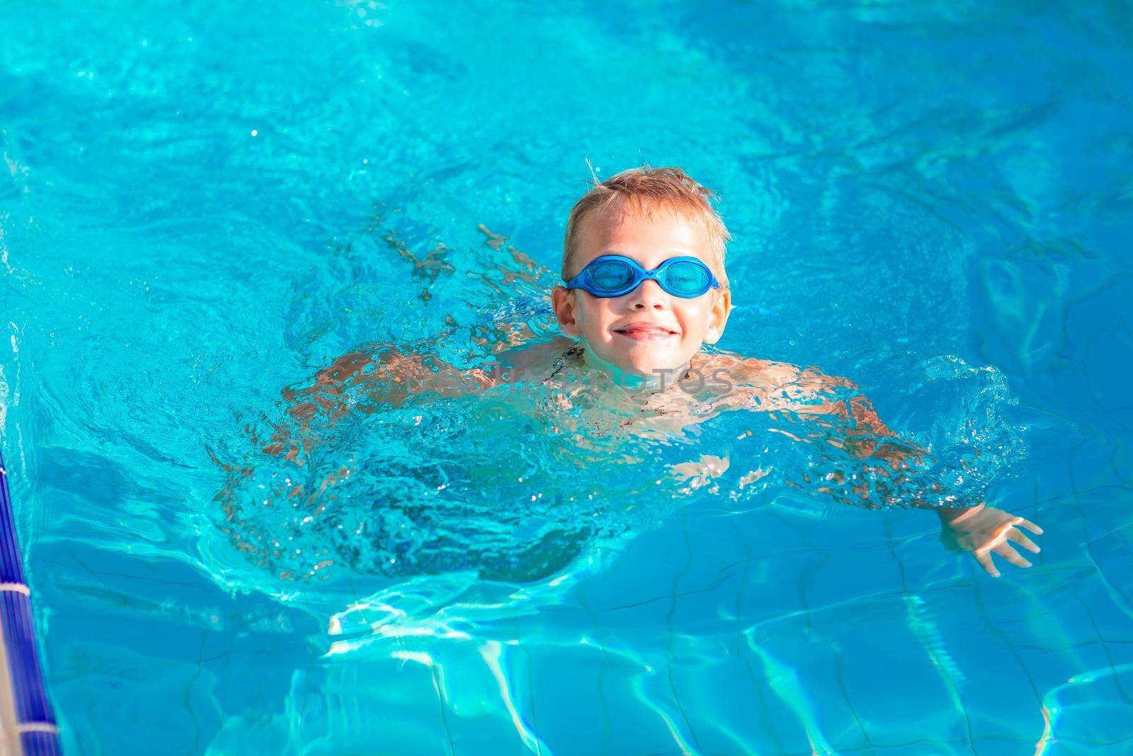 Cute happy little boy in goggles swimming and snorking in the swimming pool. Swimming for kids concept