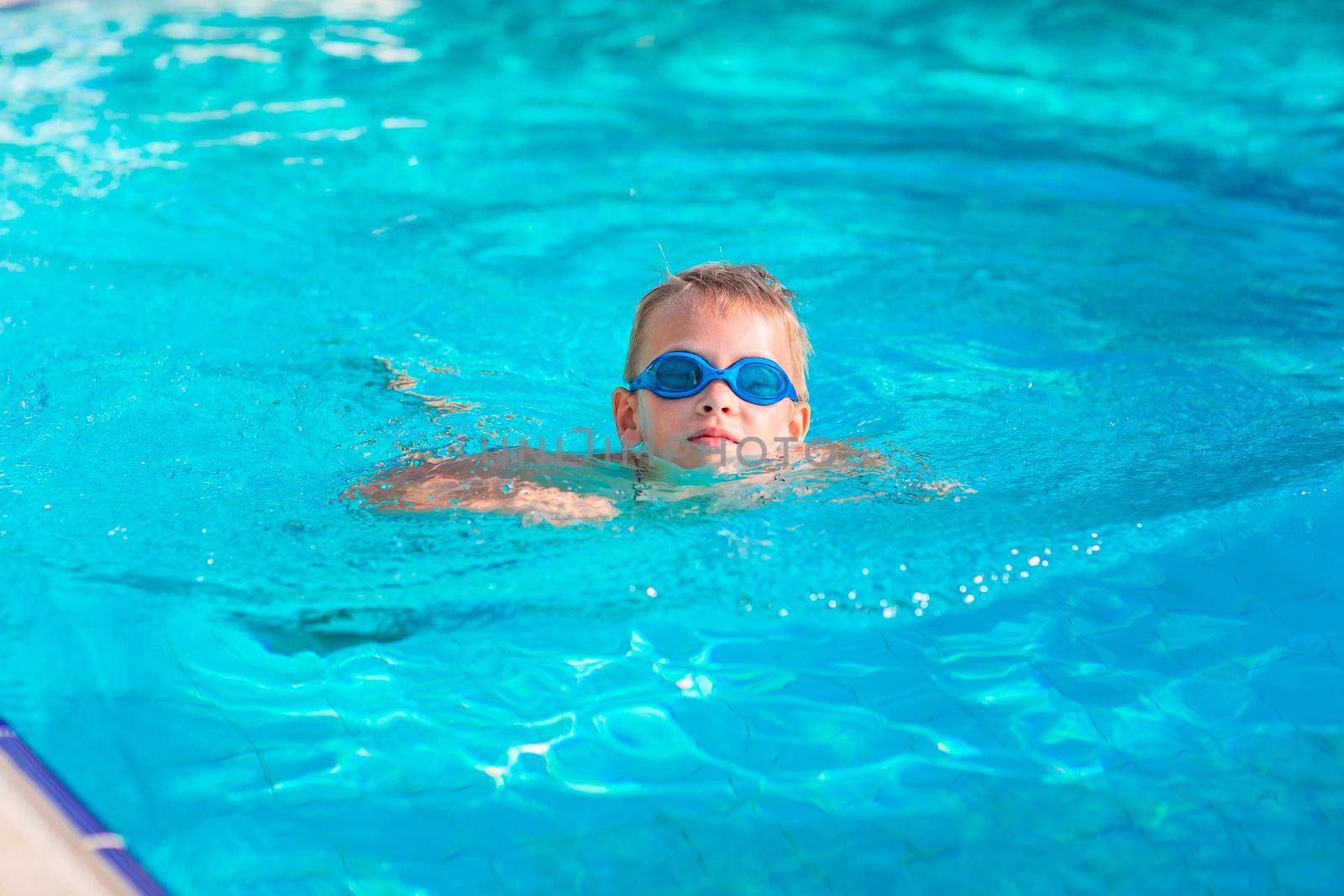 Cute happy little boy in goggles swimming and snorking in the swimming pool. Swimming for kids concept
