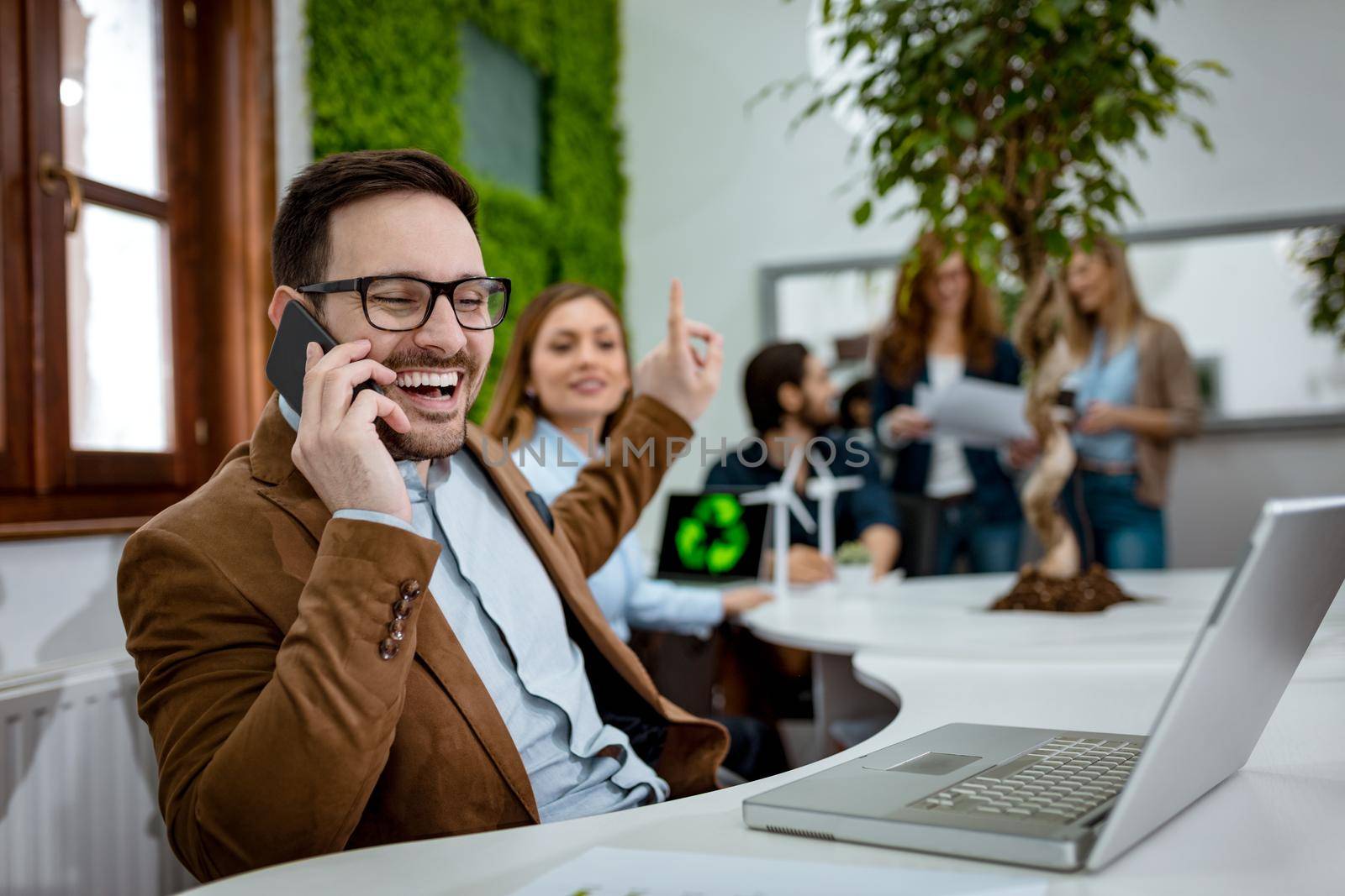 Young handsome successful smiling businessman receives good news by mobile phone and working on laptop in the office. 