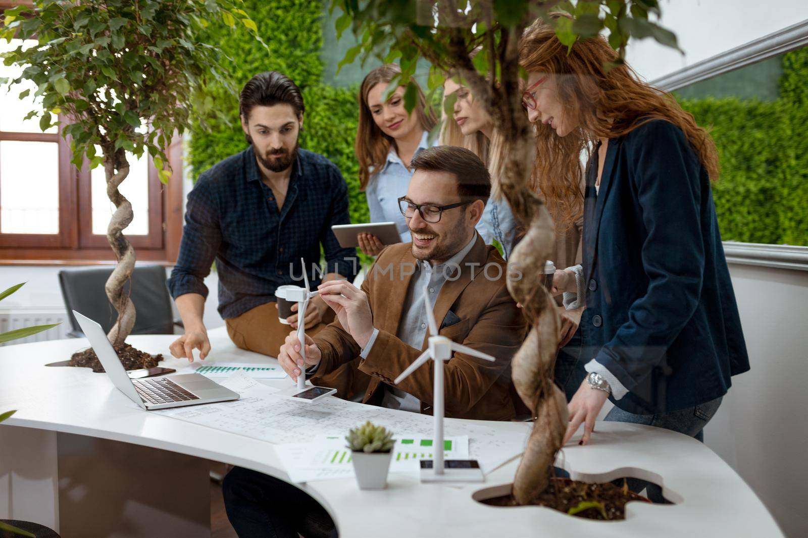 A team of a smart qualified skilled young engineers discussing about the project of alternative energy and one of them holding the tiny model of windmill turbine. 