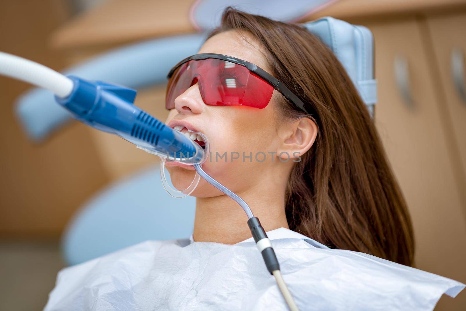 Close-up of beautiful young woman in visit at the dentist office, whitening teeth with ultraviolet light.