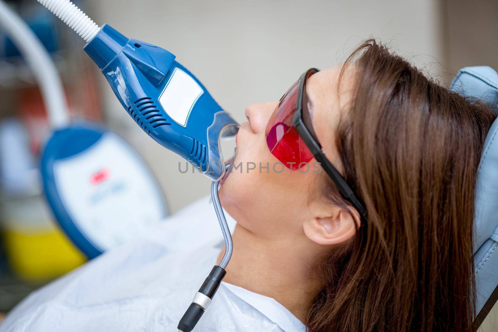 Close-up of beautiful young woman in visit at the dentist office, whitening teeth with ultraviolet light.