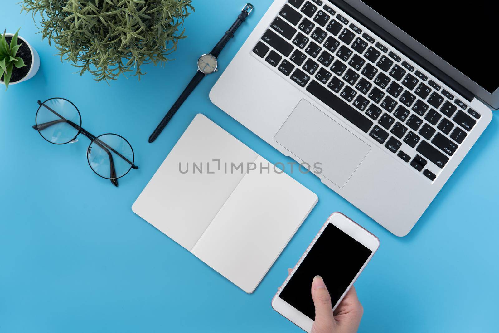 Concept of home office table with fashion accessories, minimal interior with a woman holding smartphone, flat lay, copy space, top view, mockup