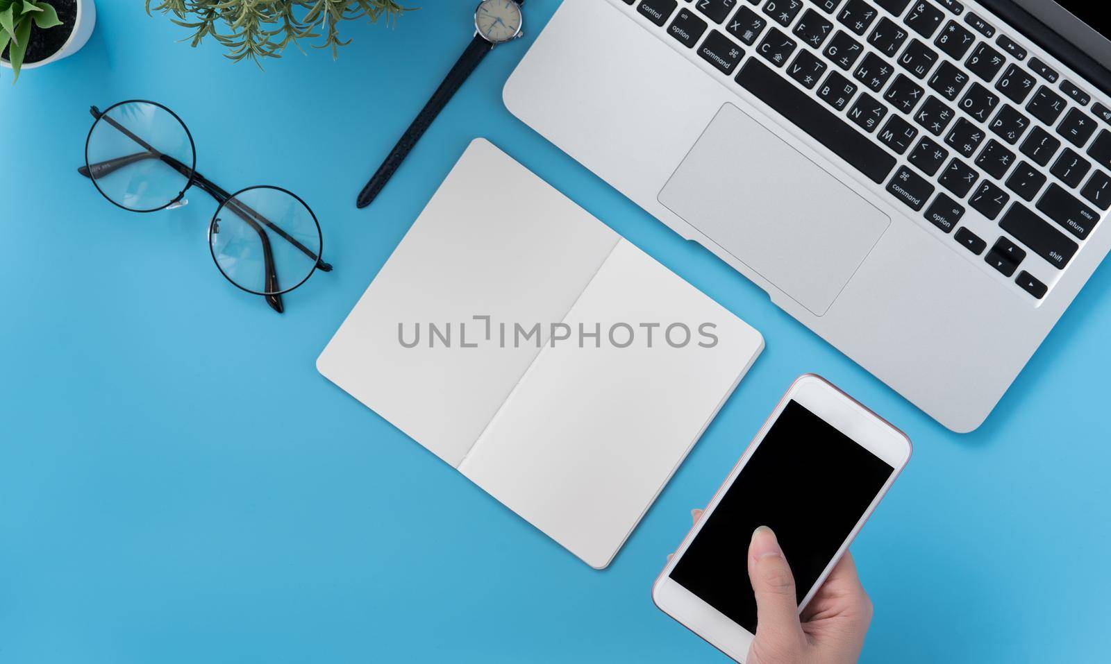 Concept of home office table with fashion accessories, minimal interior with a woman holding smartphone, flat lay, copy space, top view, mockup