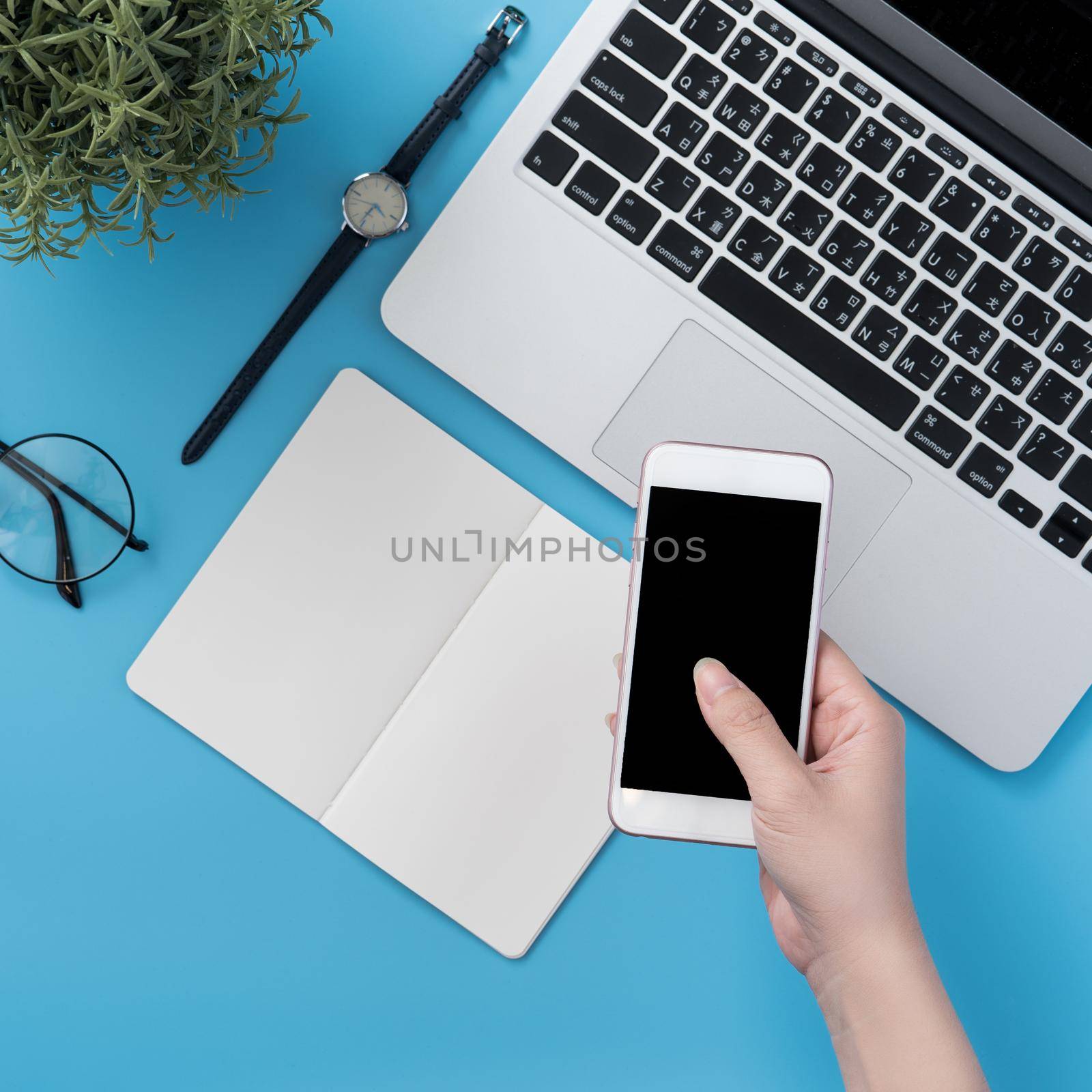 Concept of home office table with fashion accessories, minimal interior with a woman holding smartphone, flat lay, copy space, top view, mockup